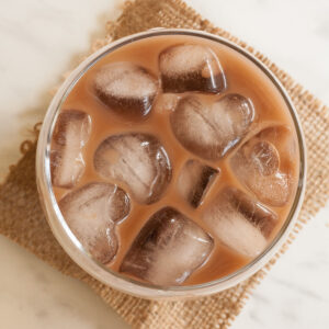 Glass from above with dark brown liquid and heart-shaped ice cubes.