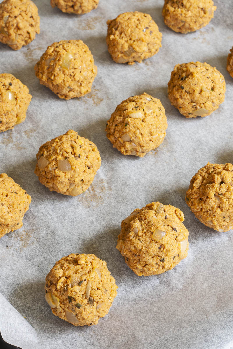 Several light brown vegan tvp meatballs on a white parchment paper before baking.