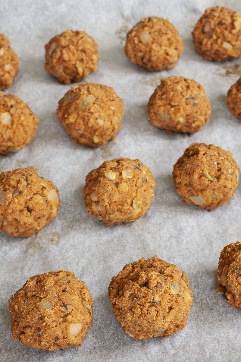 Several baked brown meatballs on a white parchment paper