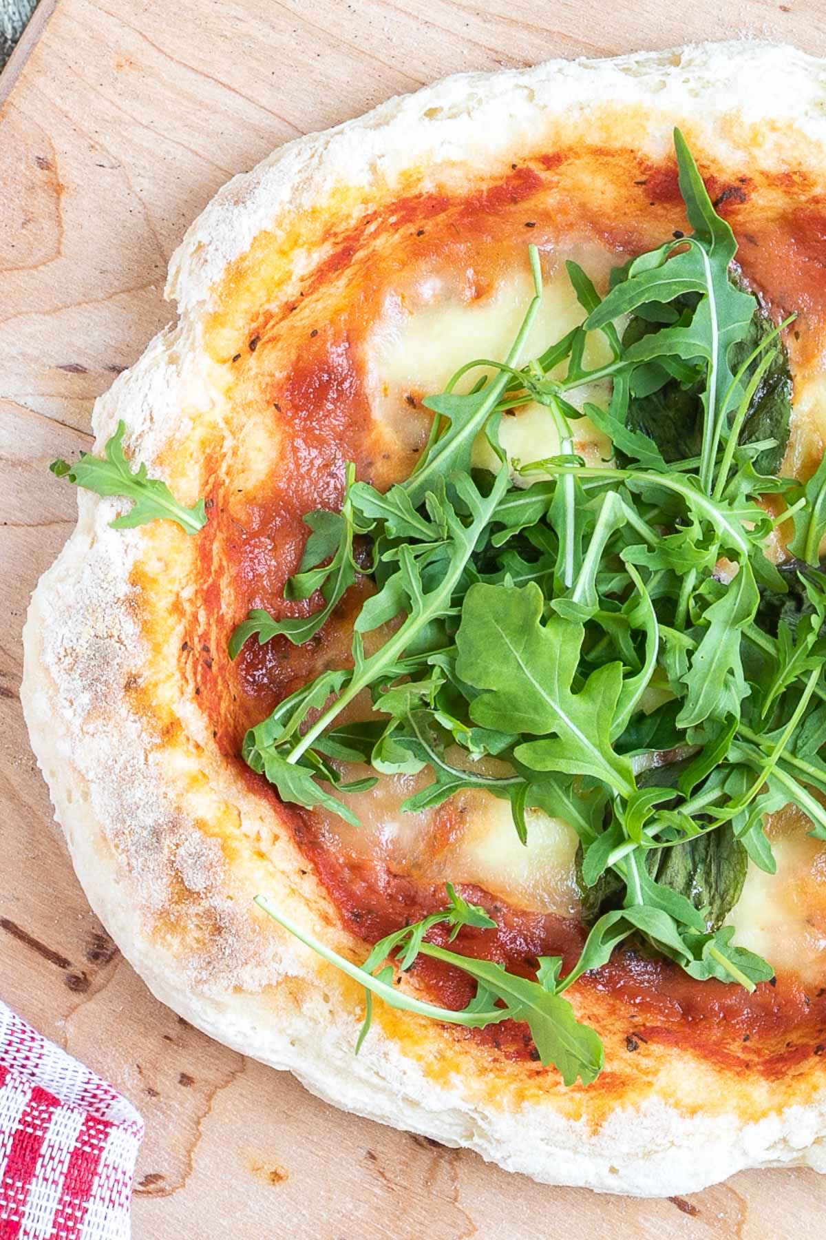Pizza with fluffy crispy crust topped with tomato sauce, melted cheese and fresh arugula on a wooden board.