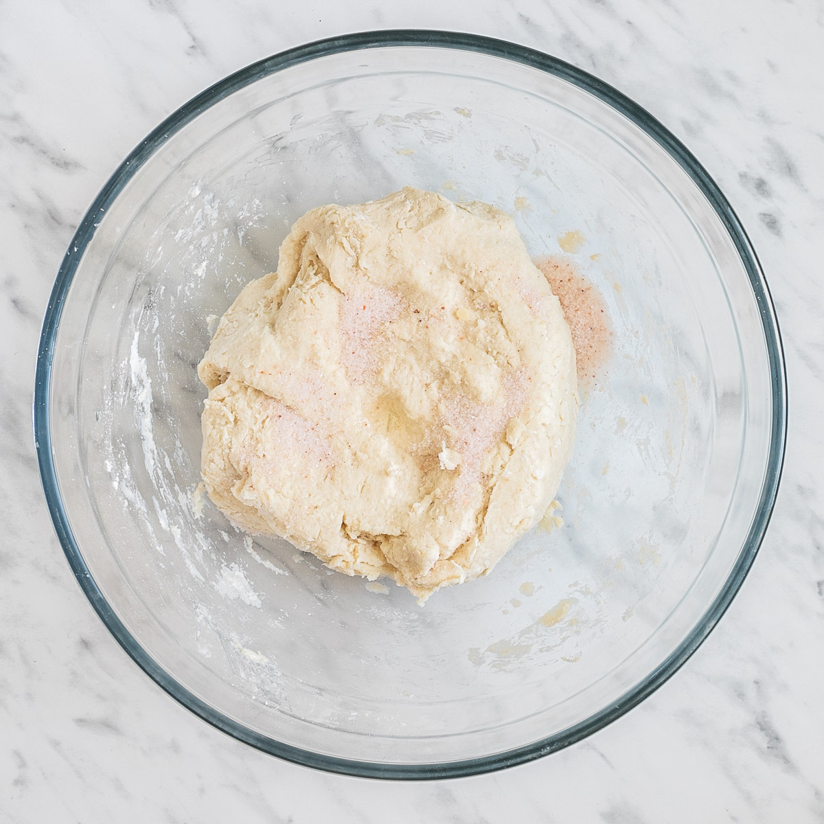 Glass bowl with a ball of dough sprinkled with salt.