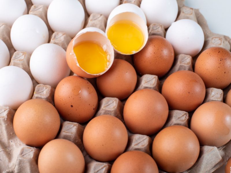 A large carton of eggs. Two cracked open and placed on the top. 