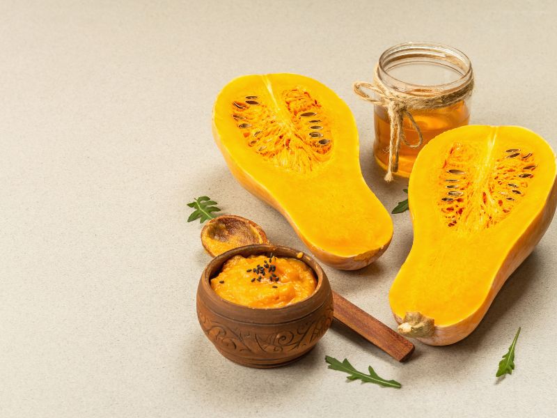 Butternut squash cut in half and some puree is placed ina wooden bowl next to it. 