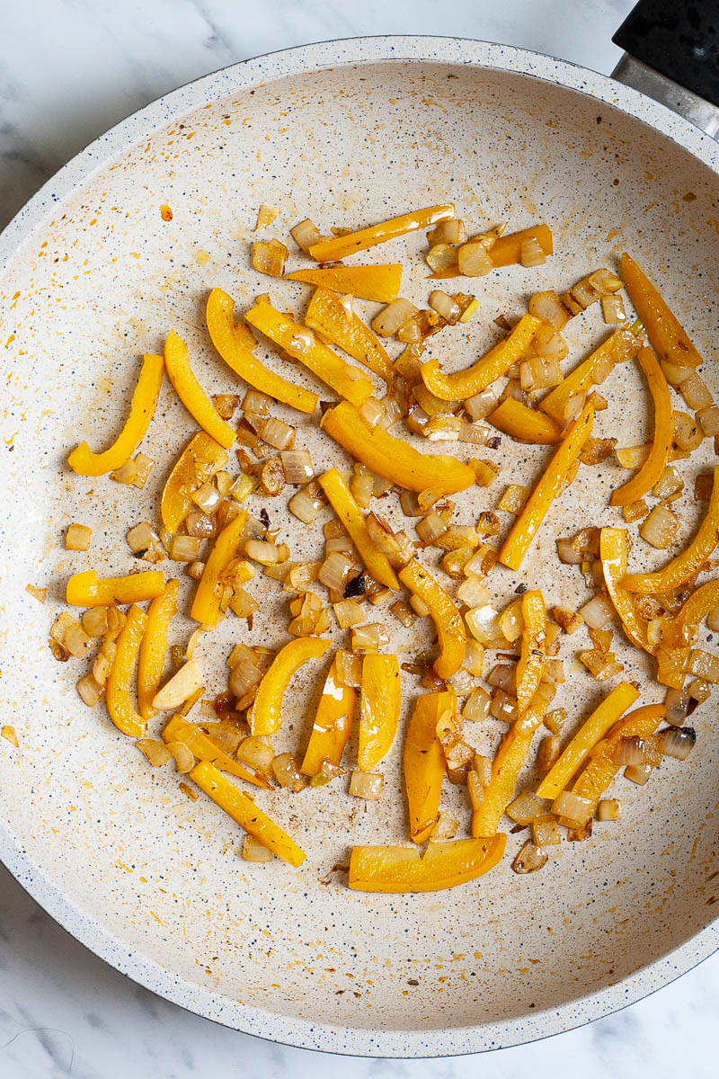Chopped onion and bell pepper slices with brownish edges in a frying pan from above.