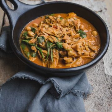 A dark brown sauce is served in a shallow black bowl with shredded mushroom, chickpeas and wilted spinach leaves