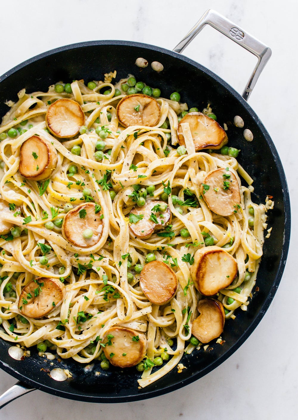 Black skillet from above with linguinie pasta round mushroom discs in creamy sauce topped with green herbs
