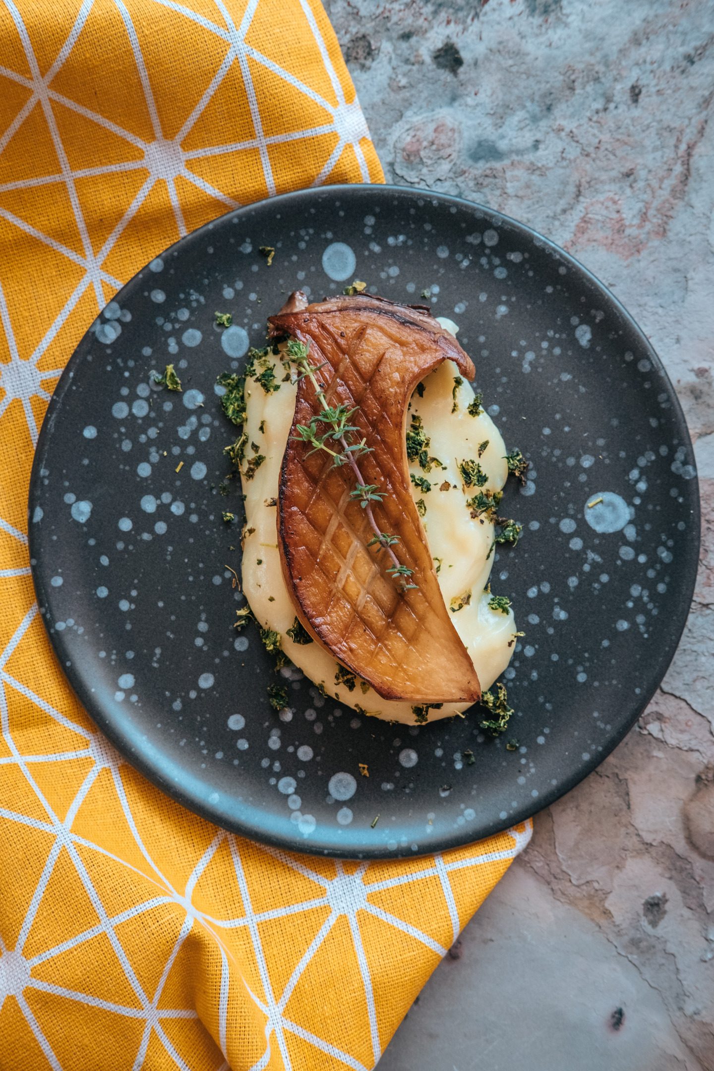 A slice of dark brown grilled king oyster mushrooms on top of a yellow mash served on a black plate.