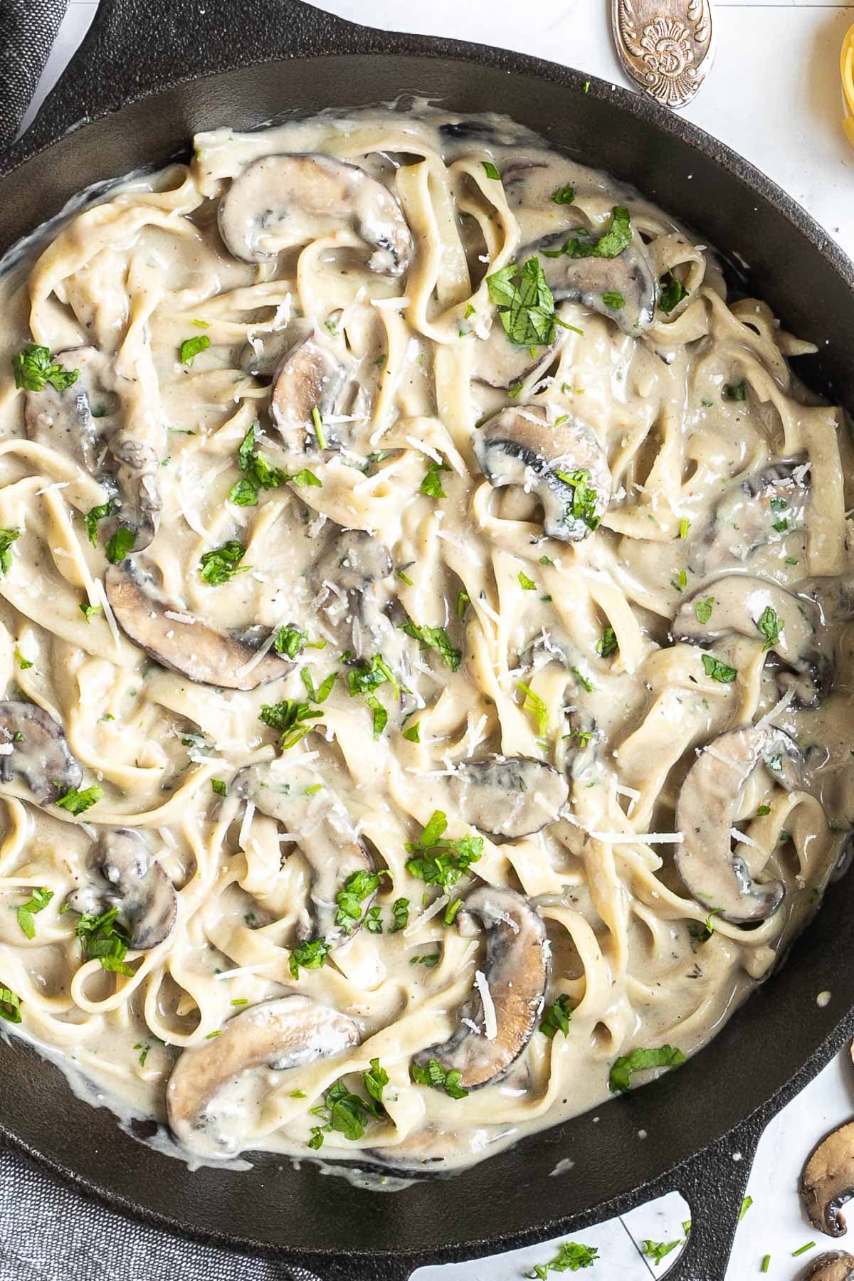 Cast iron skillet with tagliatelle in a creamy light brown sauce with sliced mushrooms and freshly chopped green herbs.