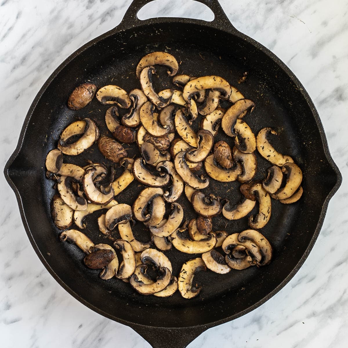 Cast iron skillet with crispy browned mushroom slices peppered with dried green herbs.