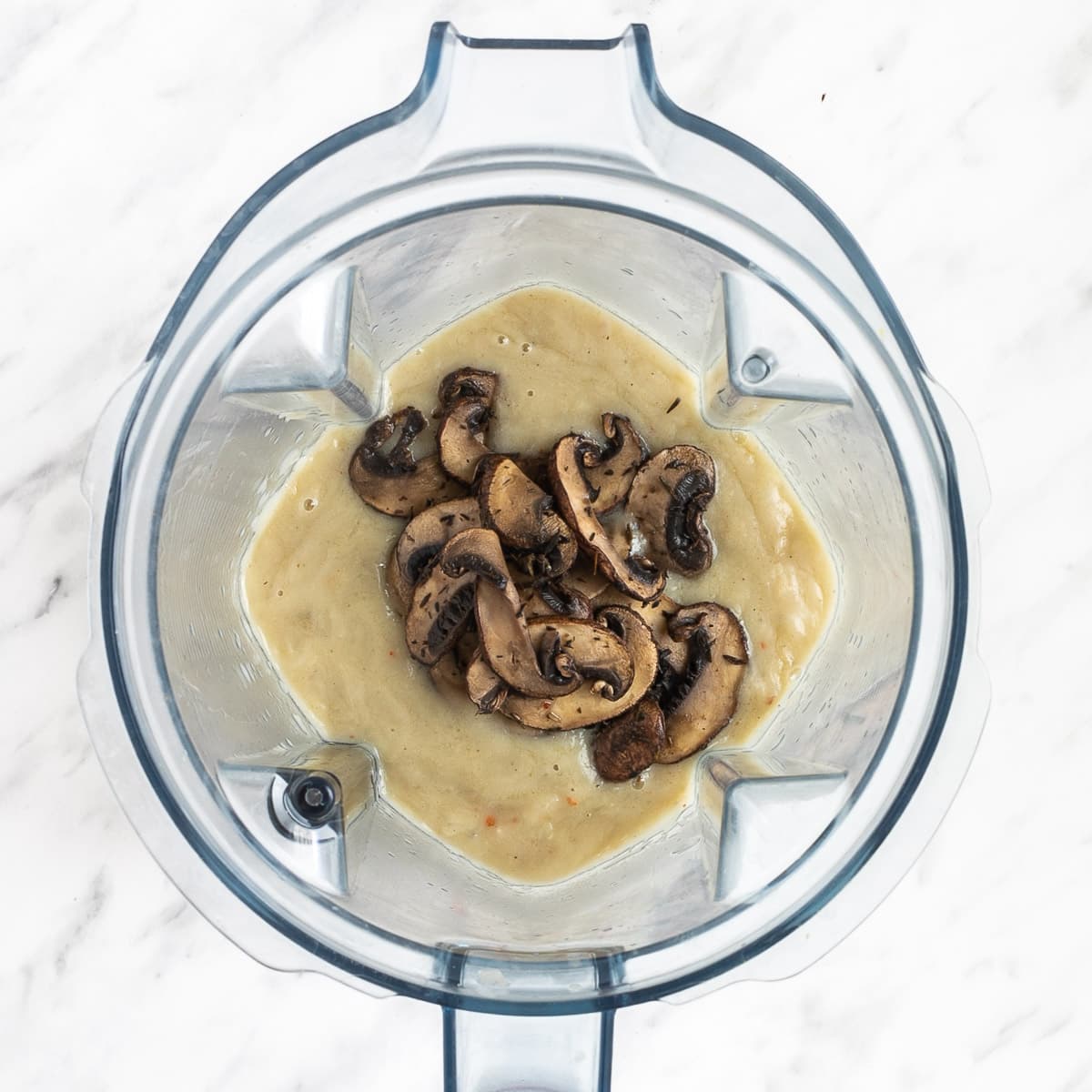 A blender with some light brown chunky sauce and crispy browned mushroom slices.