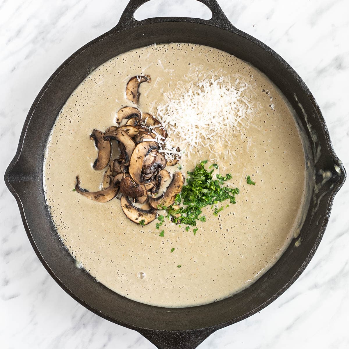Cast iron skillet with a smooth light brown sauce with crispy browned mushroom slices, grated cheese and fresh chopped parsley.