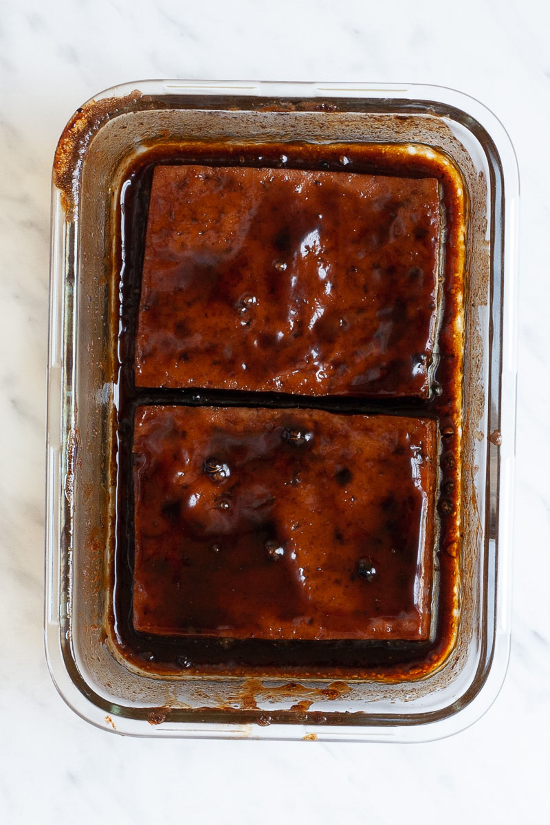 Glass bowl from above with two large tofu slices in a dark glaze-like sauce.