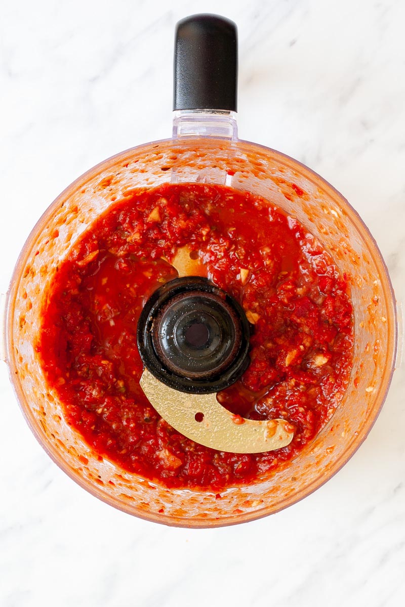 A food processor from above showing a red chunky sauce