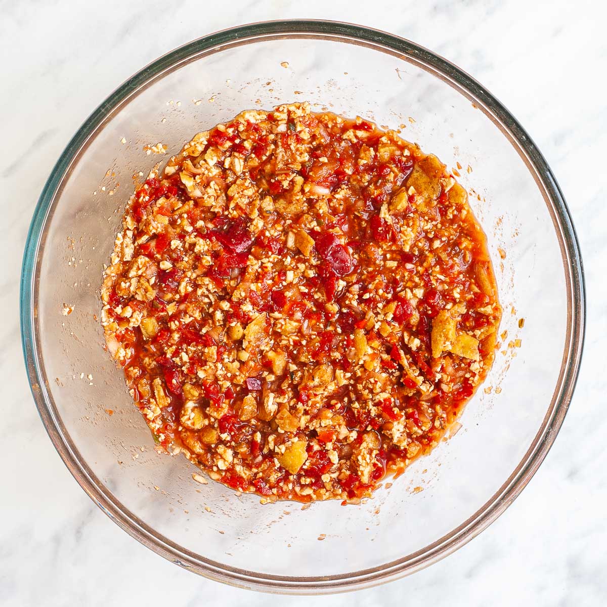 A glass mixing bowl with yellow brown pieces in a red chunky sauce.