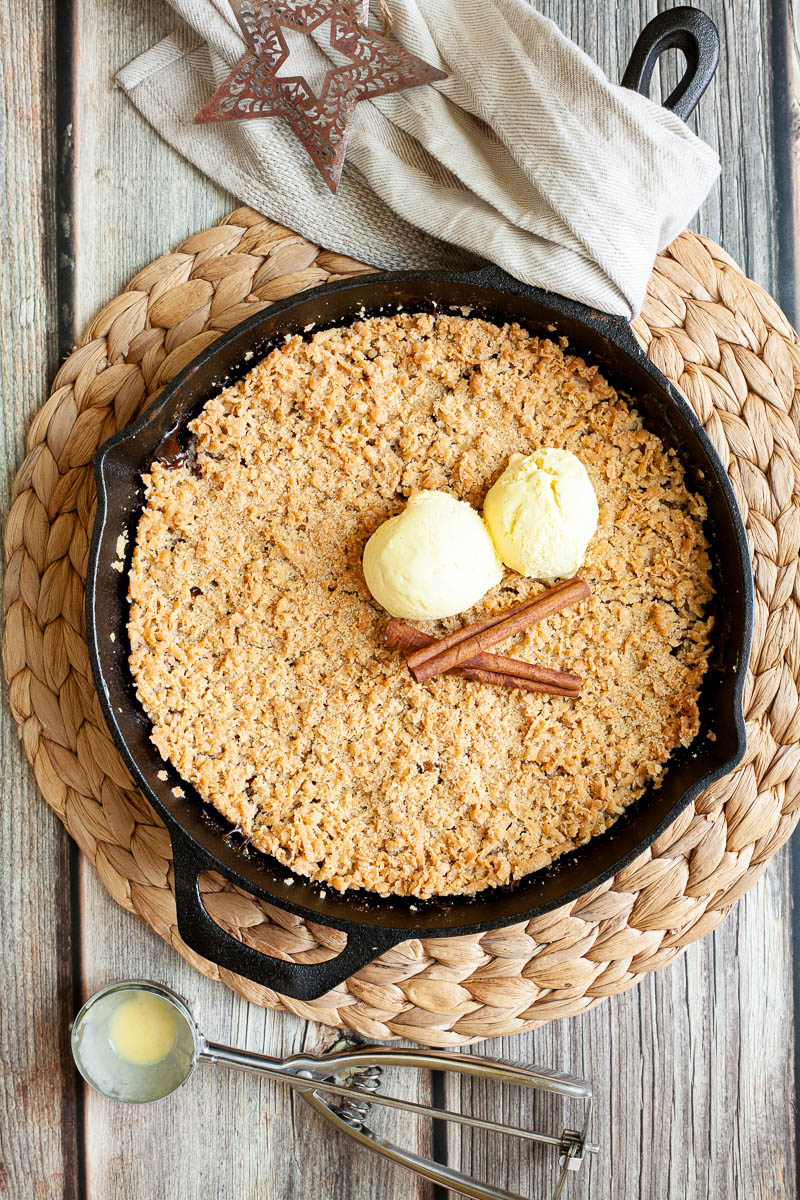 A black skillet from above full of crumble topping and 2 scoops of yellow ice cream.