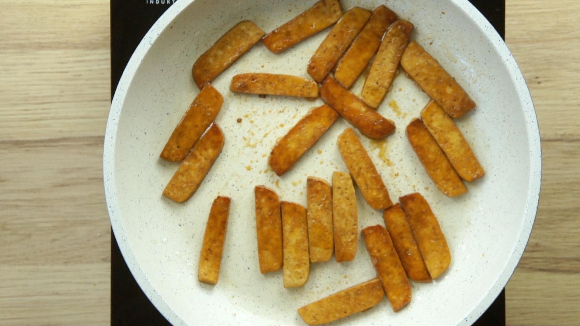 A white frying pan with crispy dark brown tofu slices.