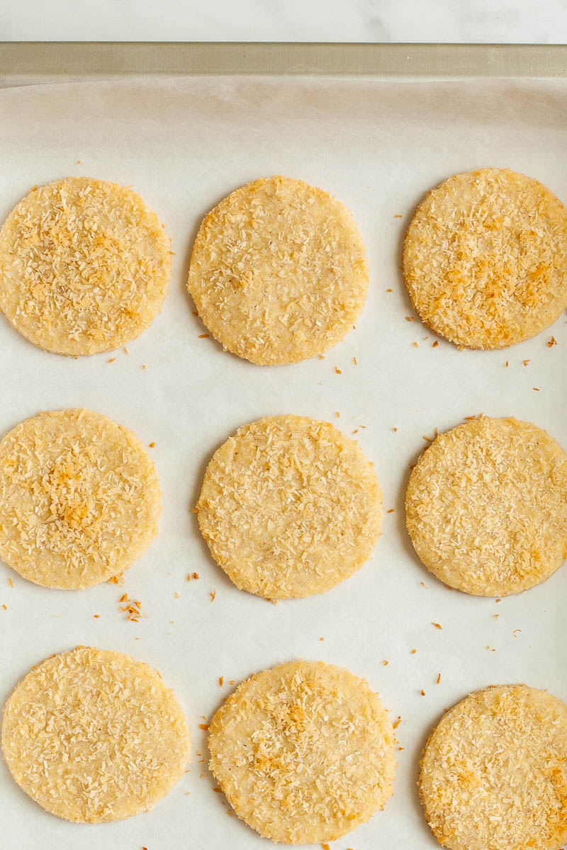 Silver baking sheet with round cookies sprinkled with shredded coconut