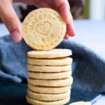 A stack of thin round cookies on a black board. A hand is holding the top cookie.