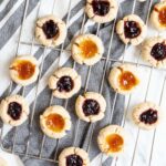 Several round cookies with orange and purple jam filling placed on a wire rack.