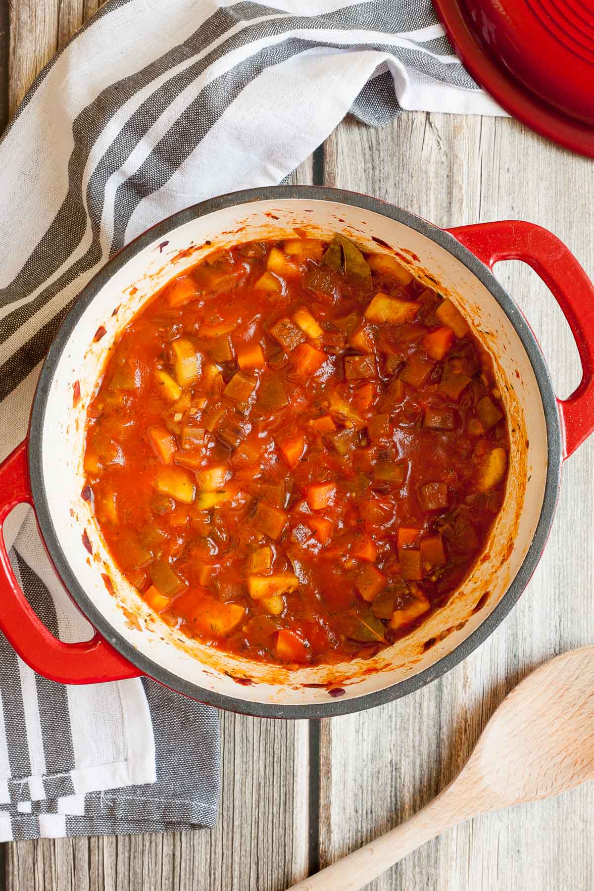 Red white enameled Dutch oven with a red thick stew full of diced vegetables. 
