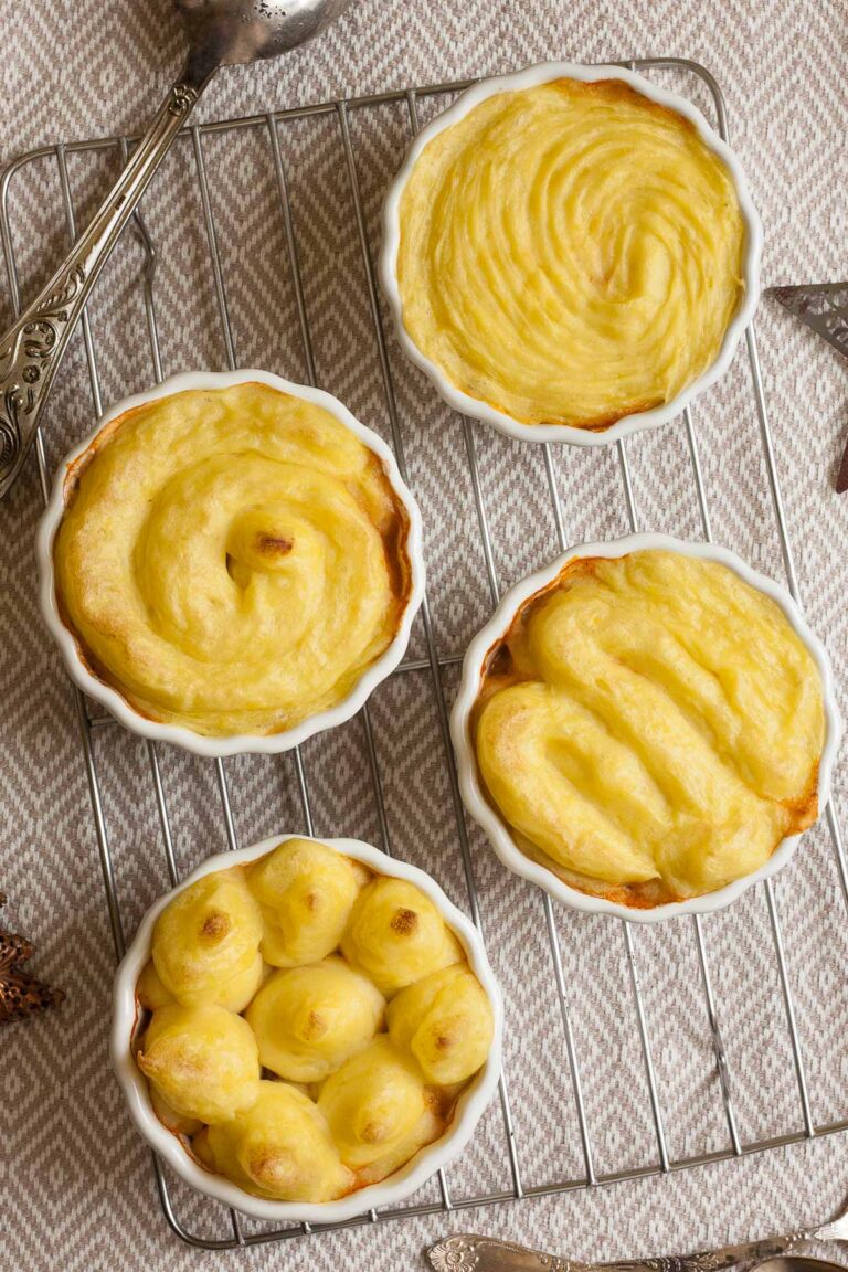 4 white ceramic pots with shepherd's pie from above but only the lovely yellow mashed potato topping is visible.