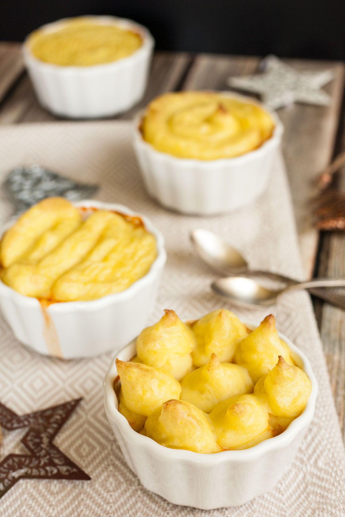 4 white ceramic pots with shepherd's pie but only the lovely yellow mashed potato topping is visible.