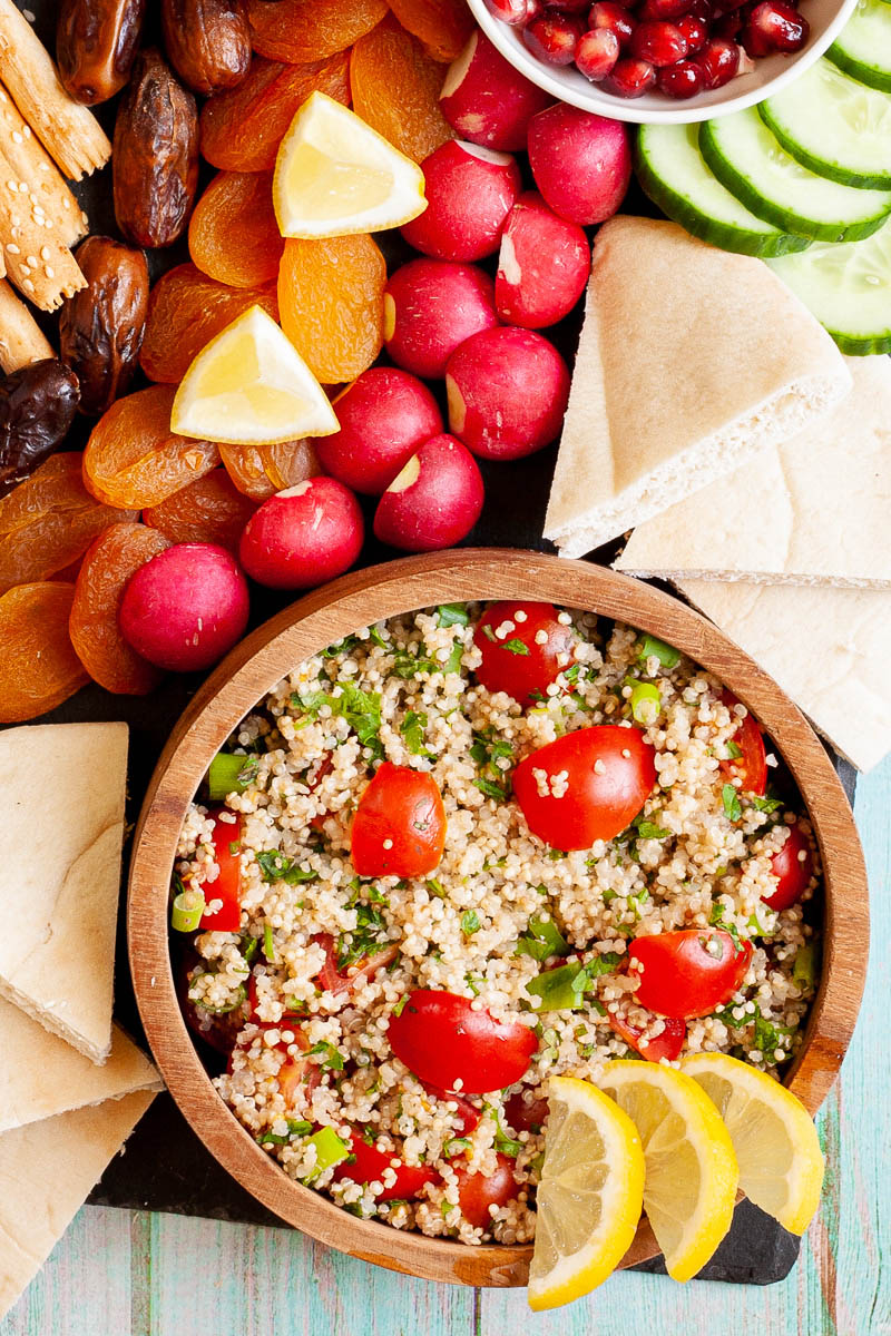 Black board with plenty of bowls, fruits and vegetables like radishes, dried apricot, pomegranate seeds, dates, tabbouleh salad