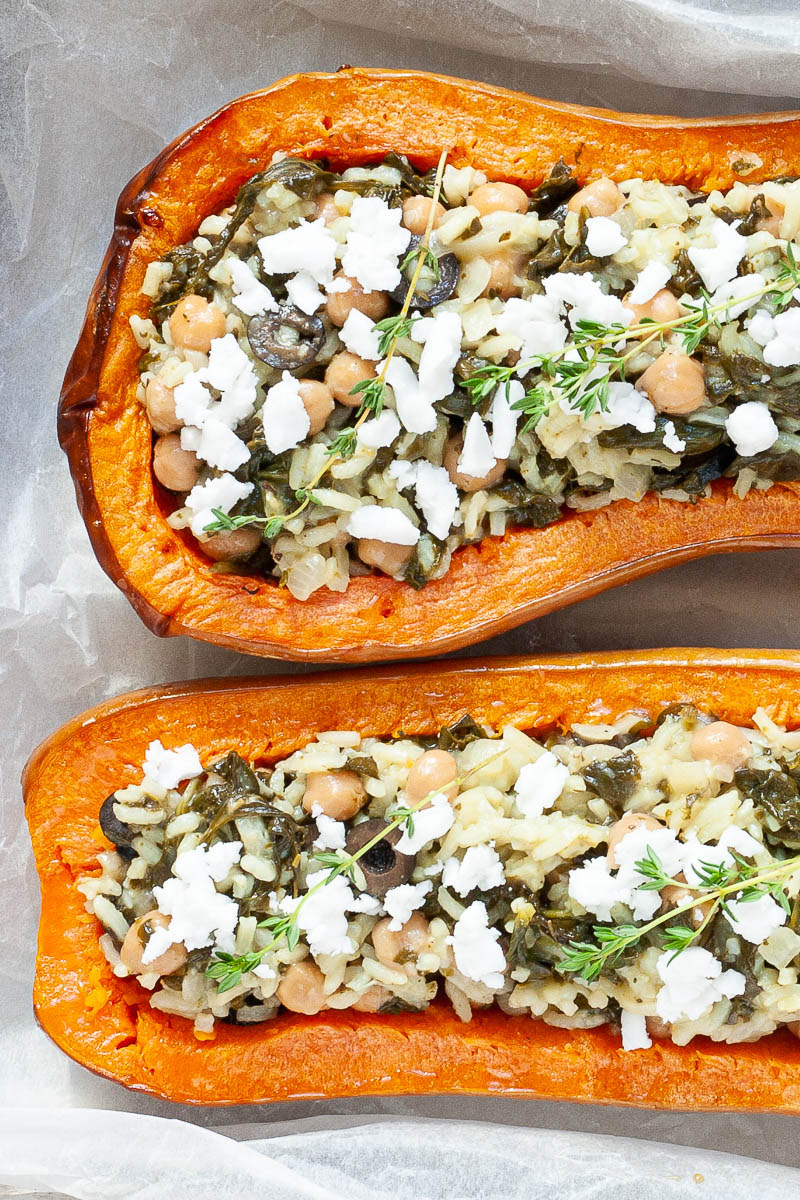 Silver baking tray with orange butternut squash cut in half and stuffed with rice, spinach, chickpeas, olives and crumbled feta cheese