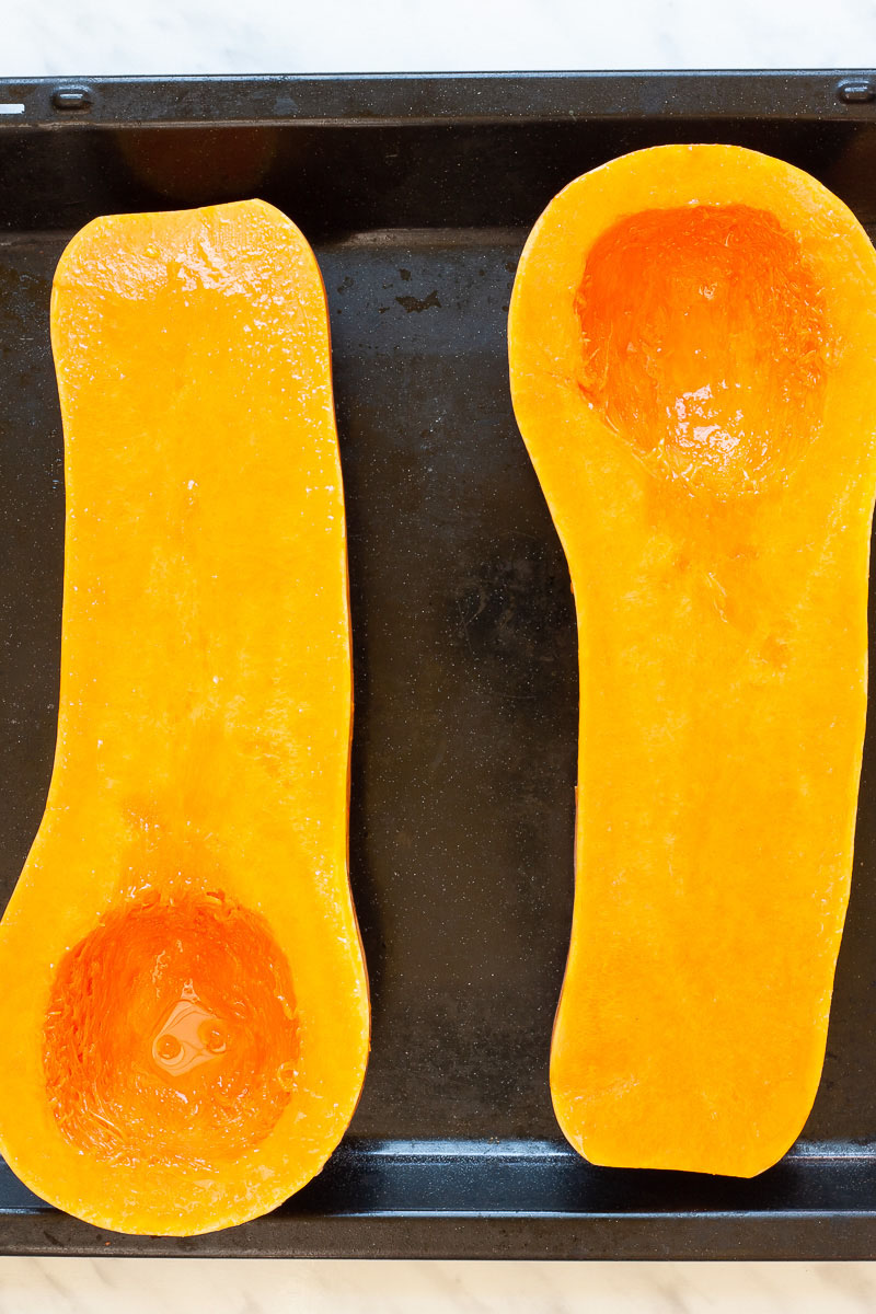 Black baking tray from above with orange butternut squash cut in half