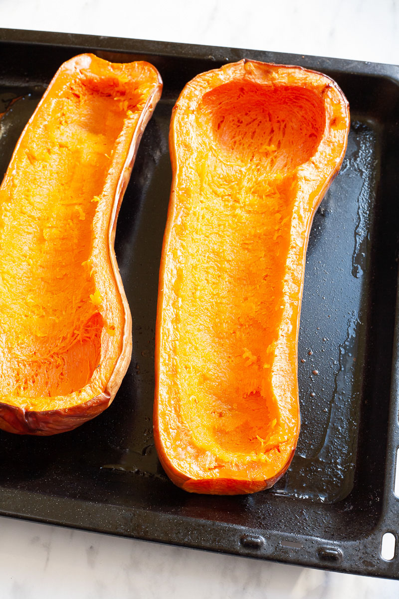 Black baking tray with 2 orange butternut squash cut in half and hollowed out
