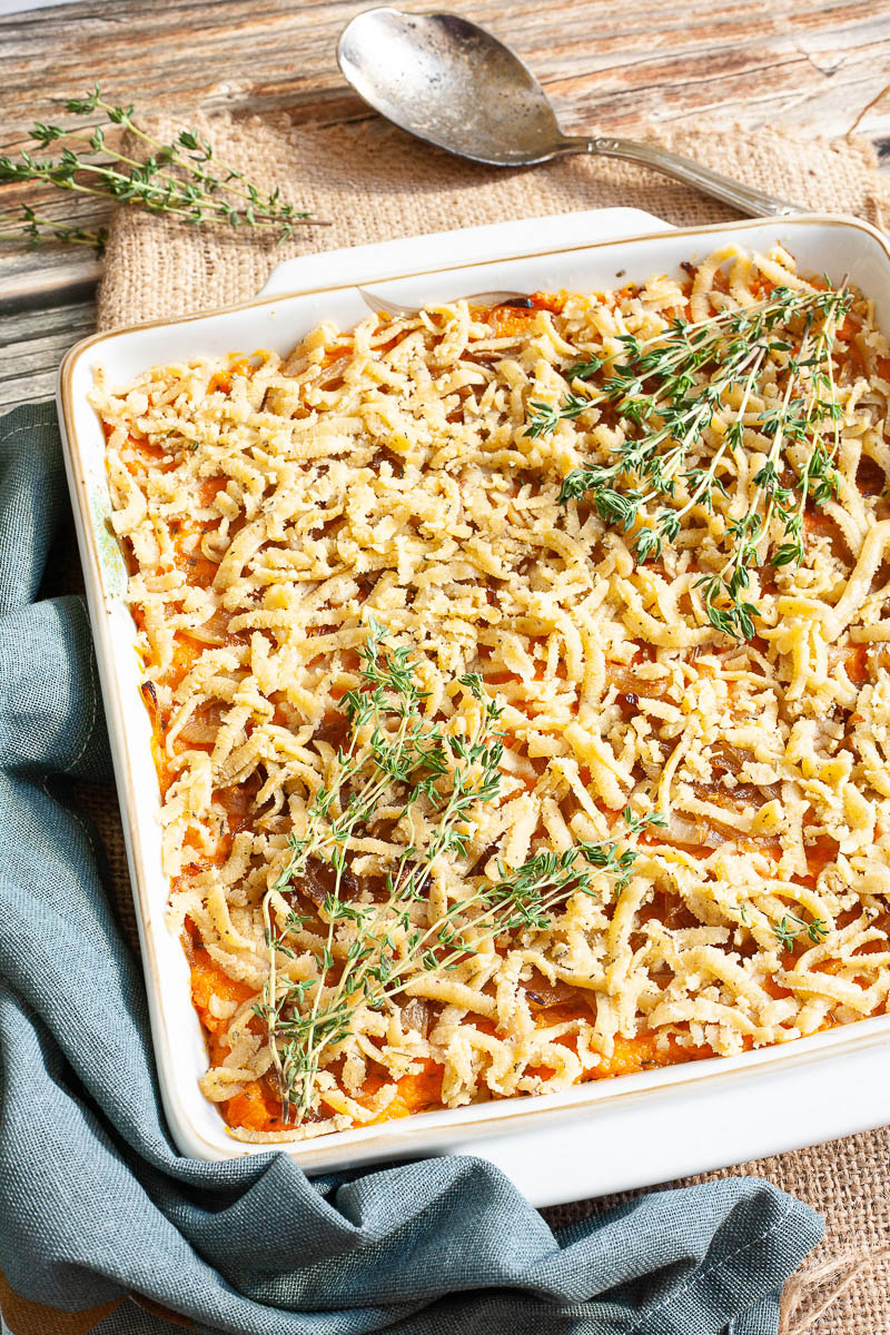 A white casserole dish from above showing orange mash topped with grated crumbles and thyme twigs.