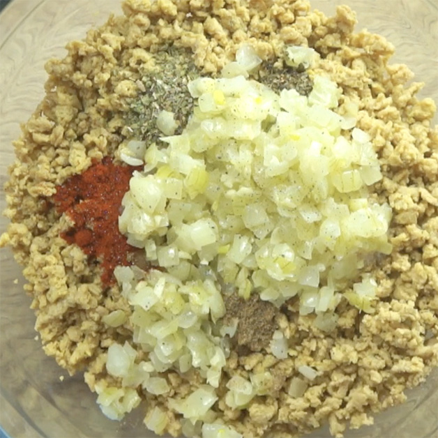 A glass bowl with light brown crumbles and 5 different spices and fried chopped onion.