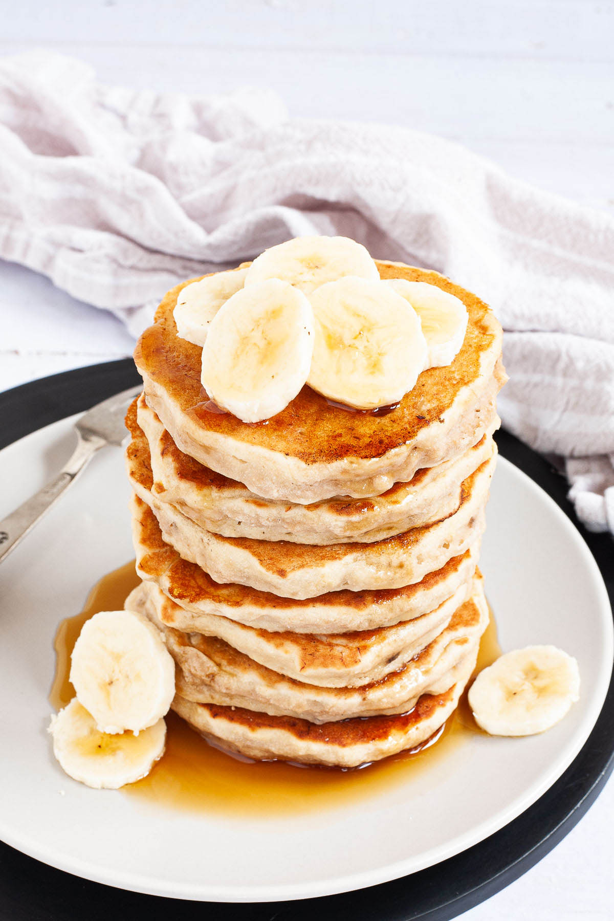 White plate with a stack of pancakes topped with banana slices