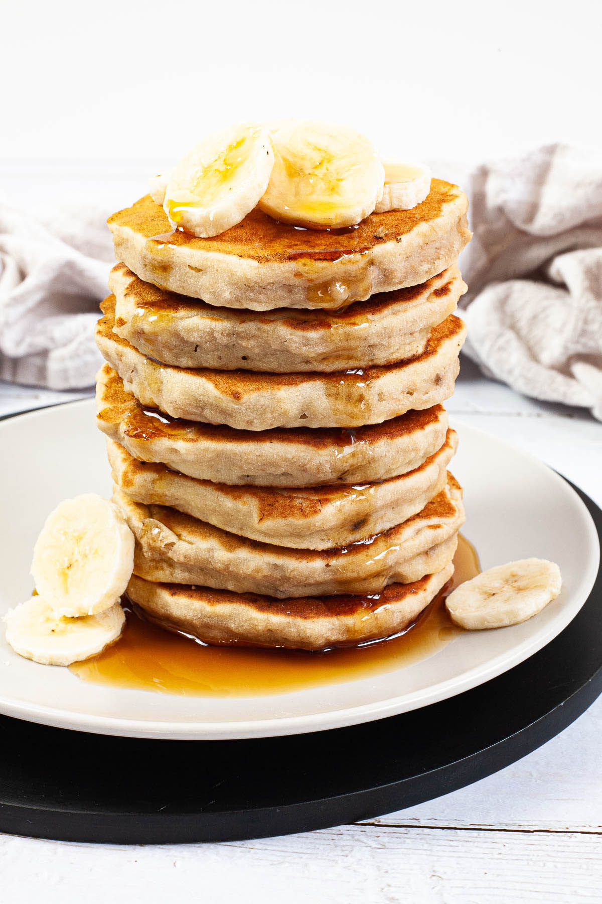 White plate with a stack of pancakes topped with banana slices