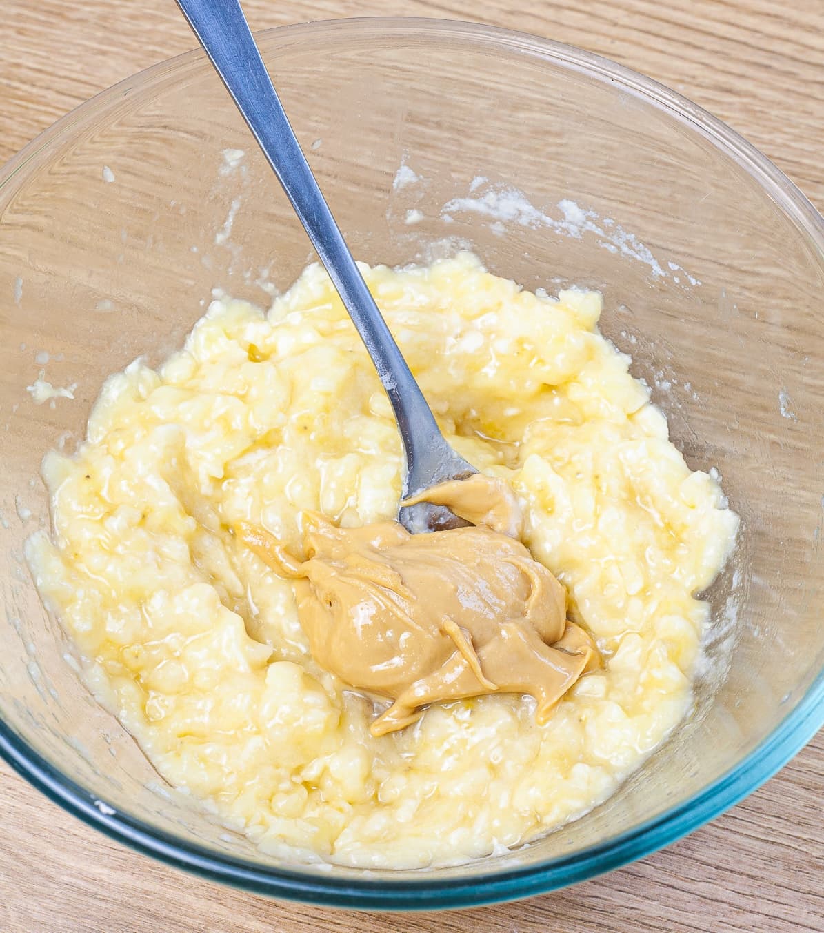 Glass bowl with mashed banana and a spoonful of peanut butter. 