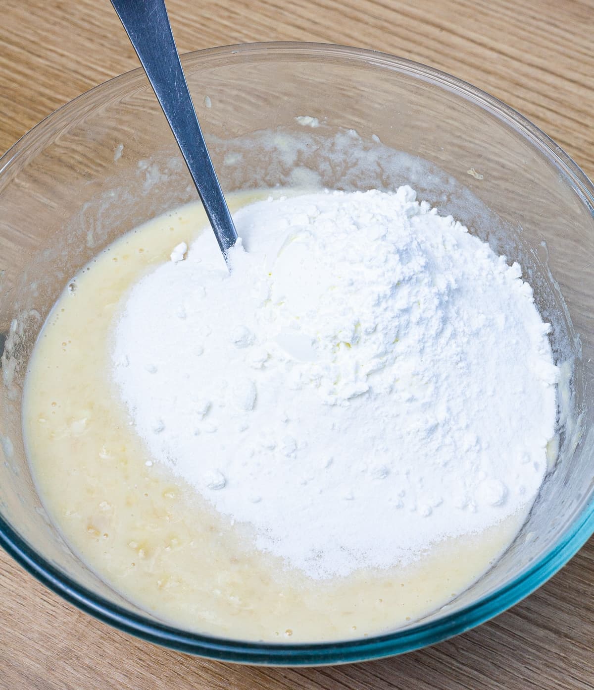 Glass bowl with a light yellow batter and a heap of white flour