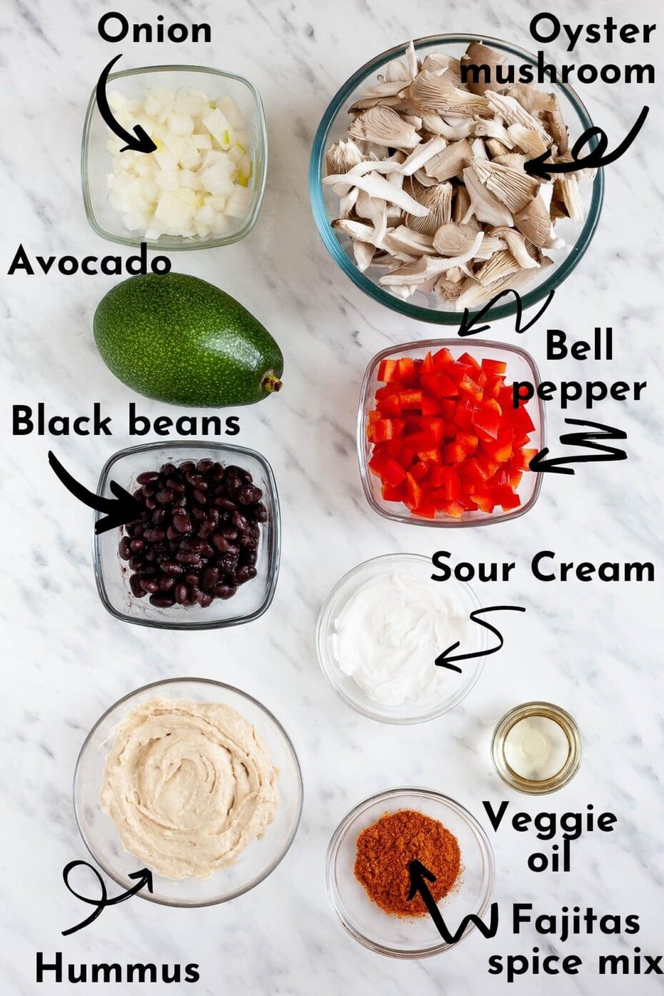 Ingredients of quesadilla in glass bowls like shredded mushroom, chopped white onion, chopped red pepper, black beans, sour cream, hummus, red spice mix and a whole avocado