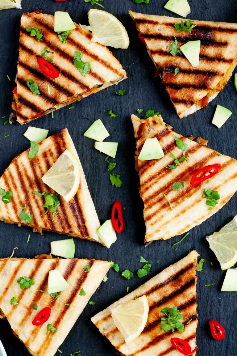 Several quesadilla triangles filled with black beans, red pepper, avocado slices sprinkled with fresh cilantro in a black board