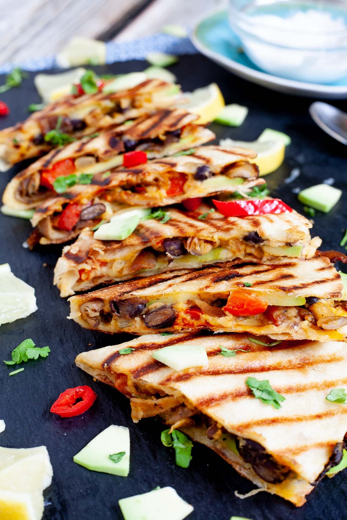 Several quesadilla triangles filled with black beans, red pepper, avocado slices sprinkled with fresh cilantro in a black board