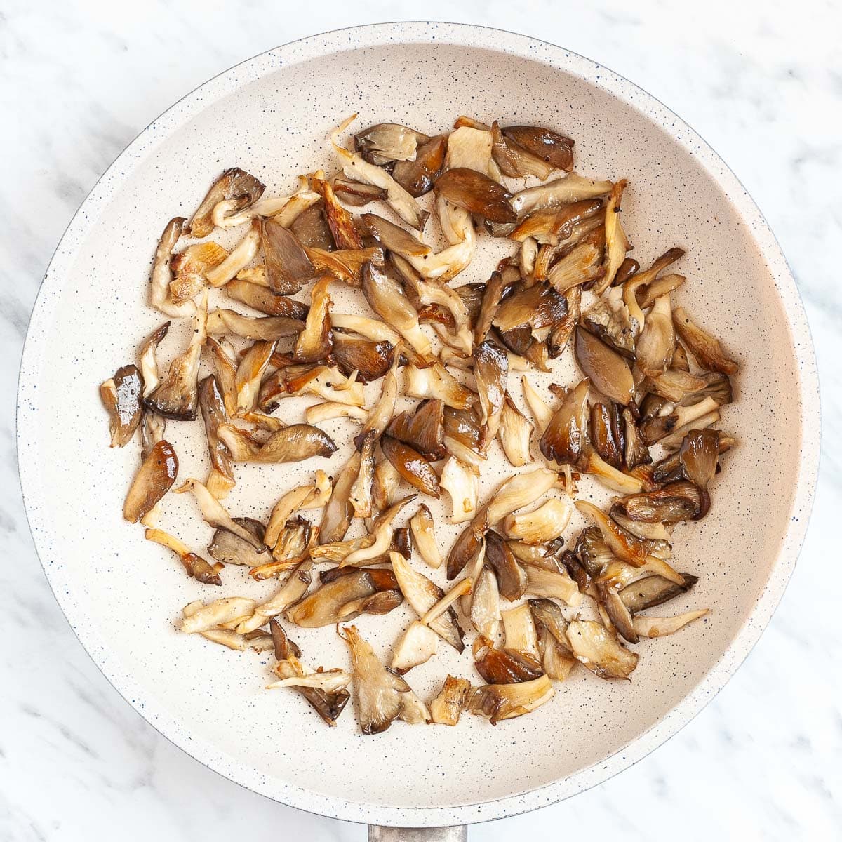 Brown mushroom shreds in a white frying pan