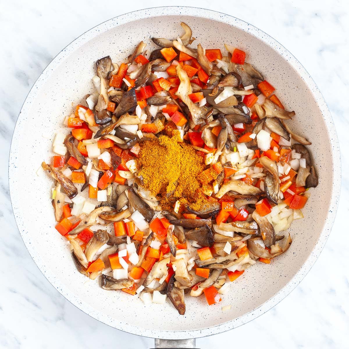 Chopped red pepper, onion and brown mushroom shreds with a spice blend in the middle in a white frying pan