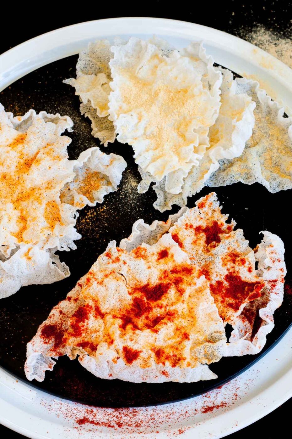 Several puffed rice paper sheets sprinkled with different spices red yellow and brownish on a black plate