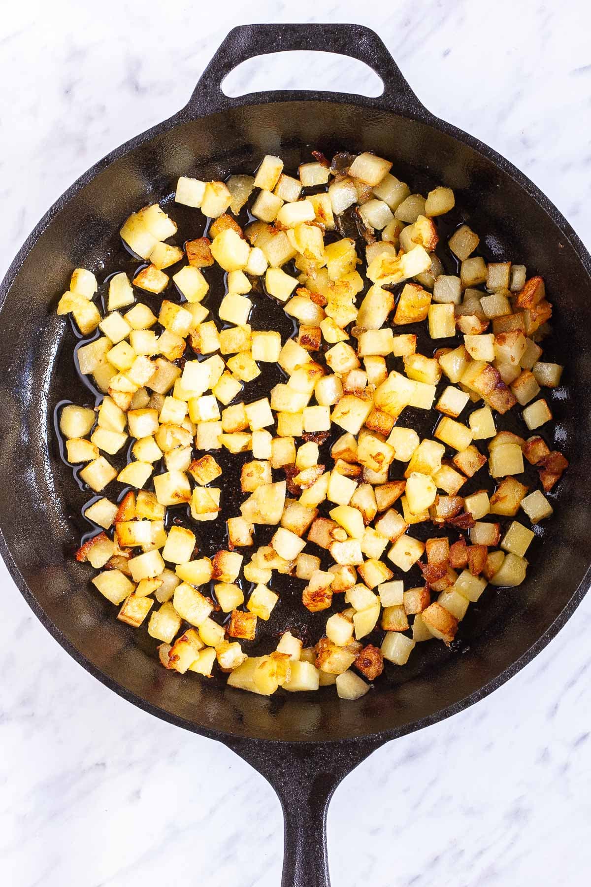 Black cast iron skillet from above with yellow diced potatoes
