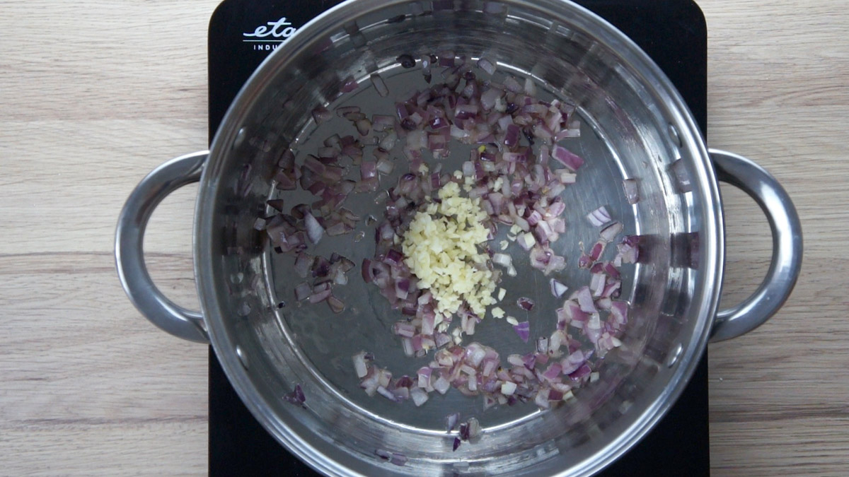 Diced red onion in pot with a small heap of minced garlic. 