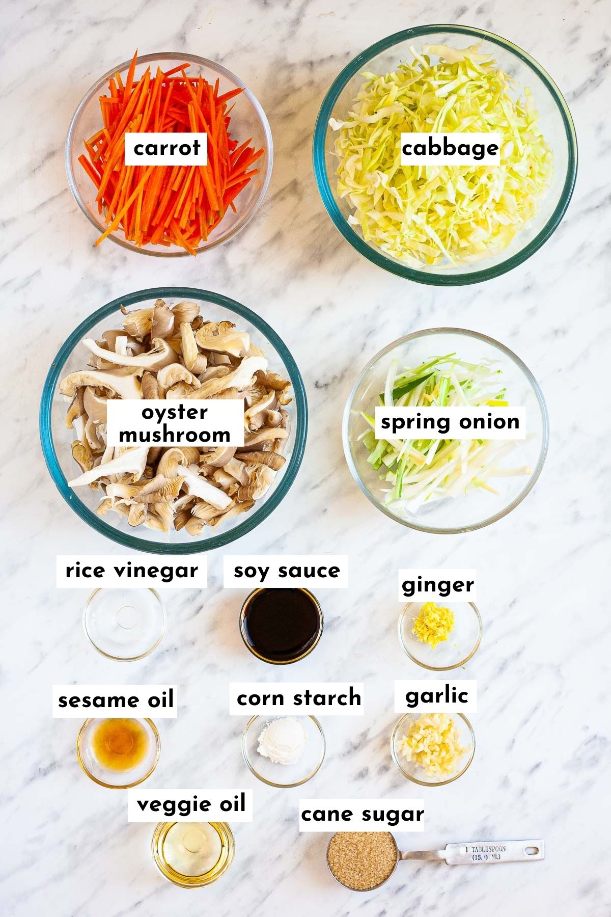 Ingredients of vegan egg rolls is placed in glass bowls like matchstick carrots, shredded cabbage, mushroom slices, spring onion slices and several spices