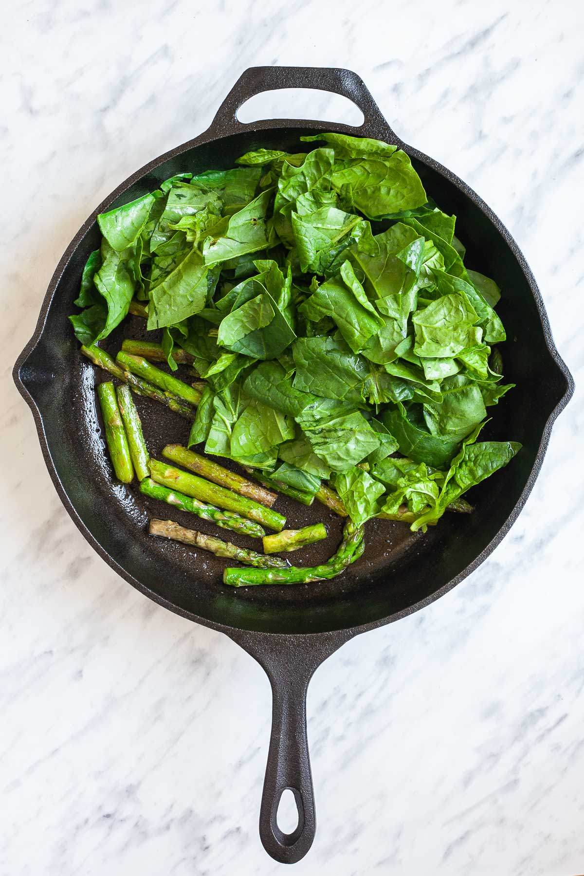 Cast iron skillet with asparagus pieces and spinach leaves.