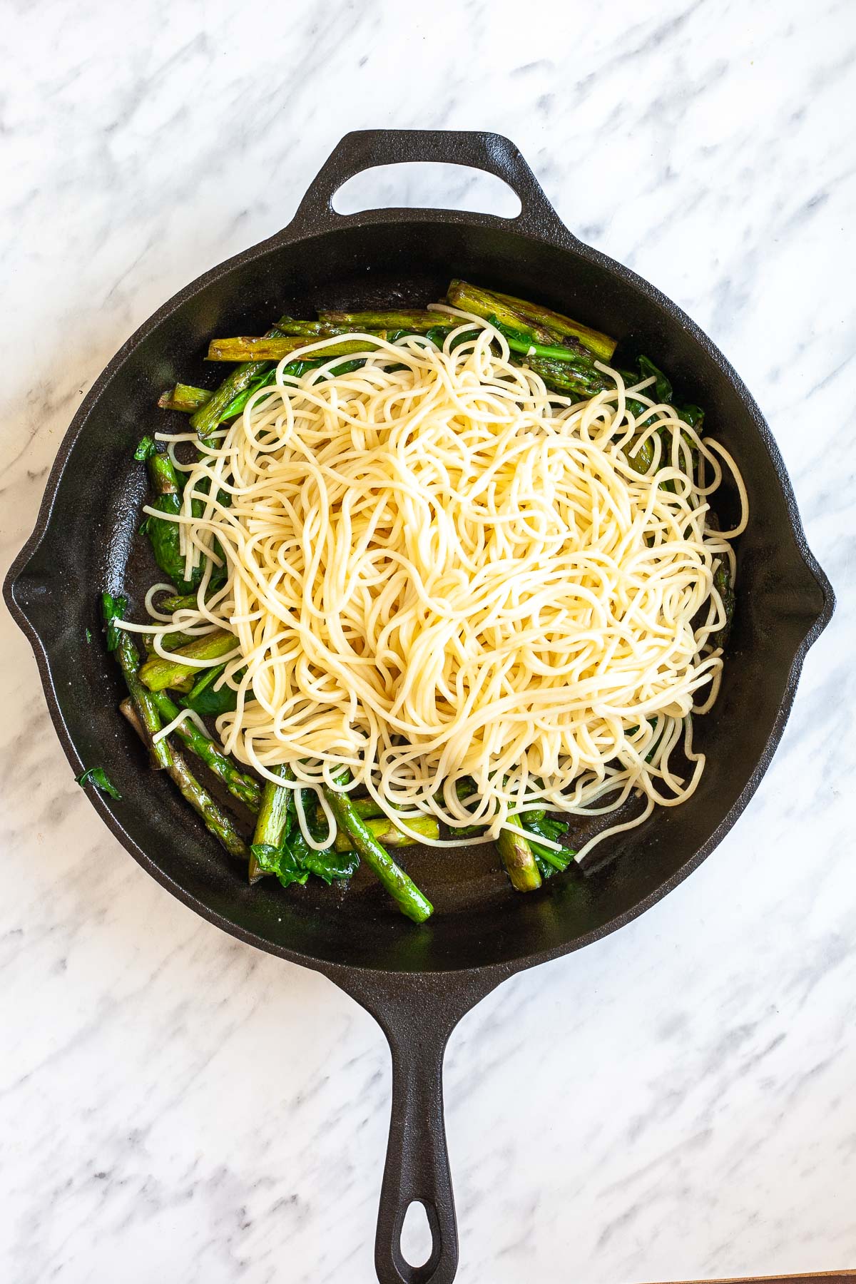 Cast iron skillet with asparagus pieces, spinach leaves, and spaghetti.