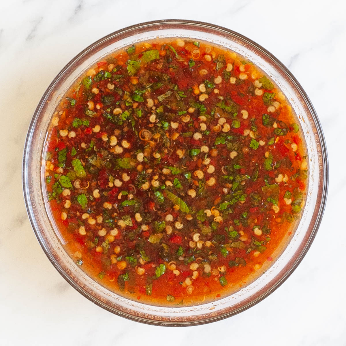 Red-brown liquid with pepper seeds, and chopped green leaves in a small glass bowl.