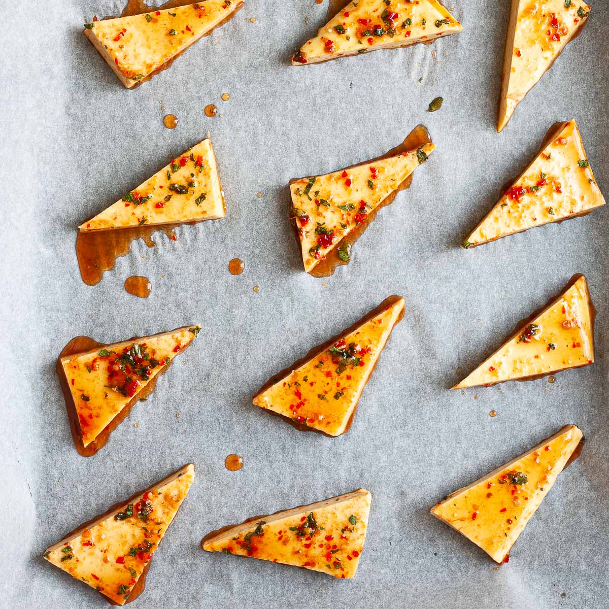 Triangle-shaped tofu on parchment paper glazed with a redish chunky marinade.