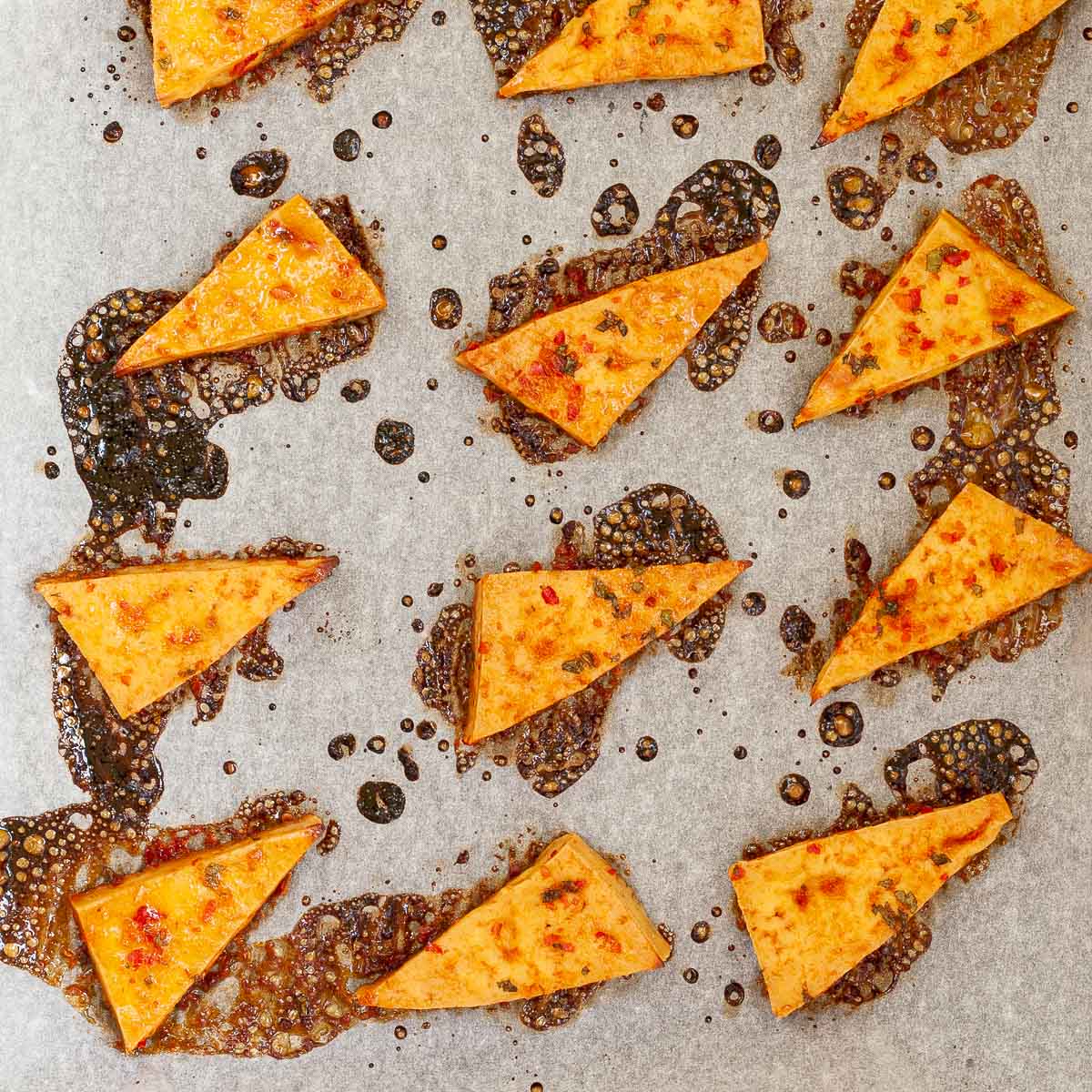 Crispy and sticky tofu triangles on parchment paper. Bubbling dark brown liquid is next to them.